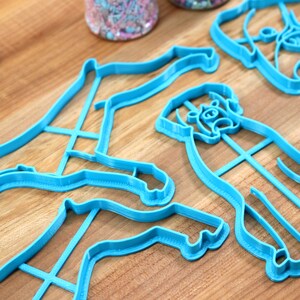 May include: Four blue plastic cookie cutters shaped like dogs. The cutters are on a wooden surface.