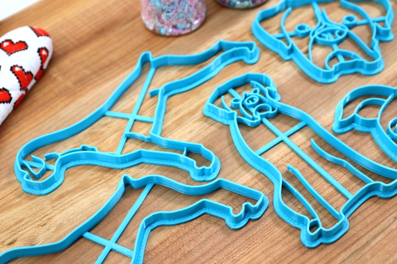May include: Four blue plastic cookie cutters shaped like dogs. The cutters are on a wooden surface.