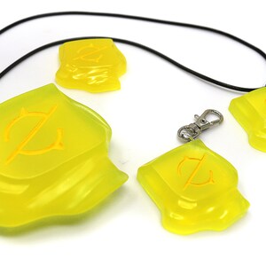 May include: A collection of translucent yellow pendants and charms. The pendants are irregularly shaped with a yellow design. One is attached to a black cord, another to a keychain clip. The other two are loose.