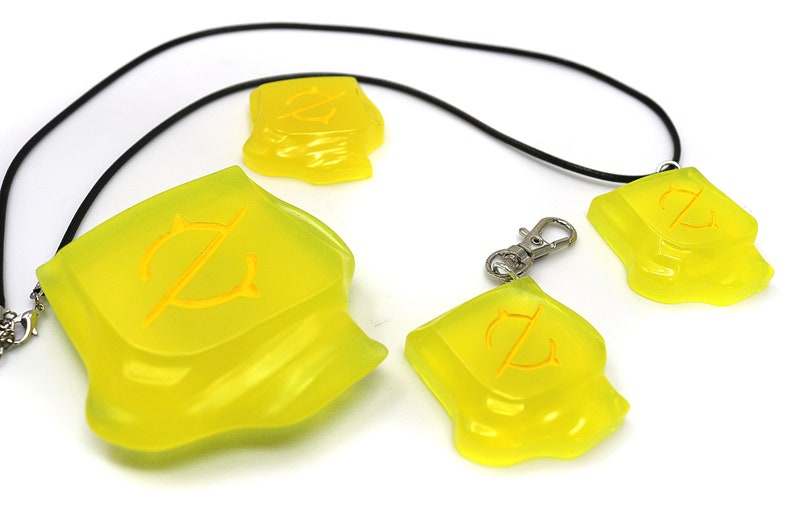 May include: A collection of translucent yellow pendants and charms. The pendants are irregularly shaped with a yellow design. One is attached to a black cord, another to a keychain clip. The other two are loose.