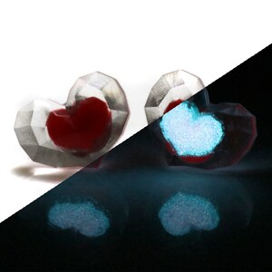 Puede incluir: Dos adornos de vidrio en forma de coraz&oacute;n con un interior rojo. Los adornos brillan en azul en la oscuridad.