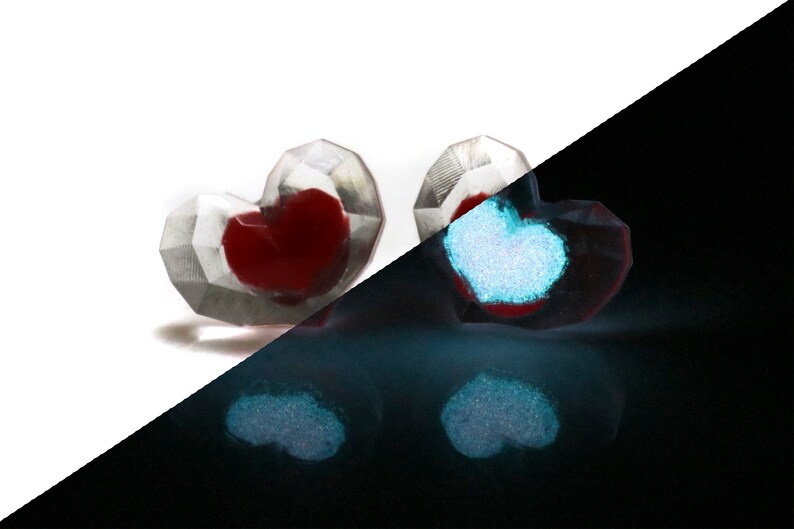 Puede incluir: Dos adornos de vidrio en forma de coraz&oacute;n con un interior rojo. Los adornos brillan en azul en la oscuridad.