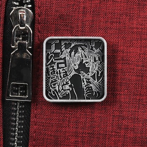 Puede incluir: Un pin de metal plateado con una imagen en blanco y negro de una mujer con el pelo largo. El pin tiene texto japon&eacute;s alrededor de la imagen.