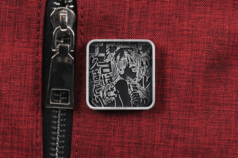 Puede incluir: Un pin de metal plateado con una imagen en blanco y negro de una mujer con el pelo largo. El pin tiene texto japon&eacute;s alrededor de la imagen.