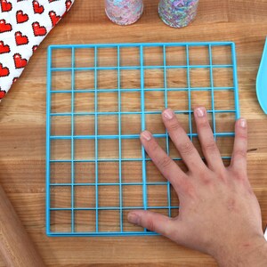 May include: A blue plastic baking sheet with a grid pattern. The sheet is 12 inches by 12 inches and has 36 squares.