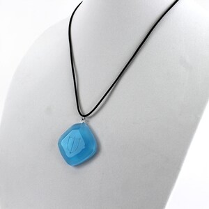 May include: A blue glass pendant with a silver chain on a black cord necklace. The pendant is shaped like a diamond and has a design etched into it.