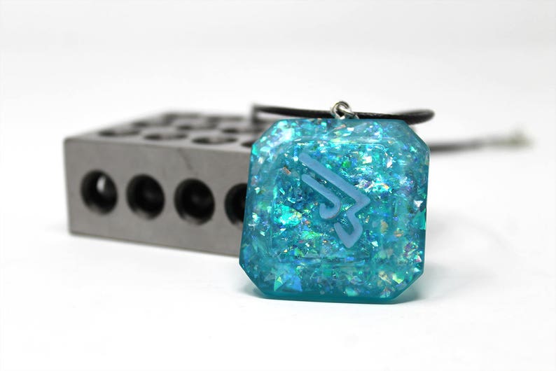 May include: A turquoise blue pendant necklace with a silver chain and a clear resin pendant with a white geometric design and iridescent glitter.