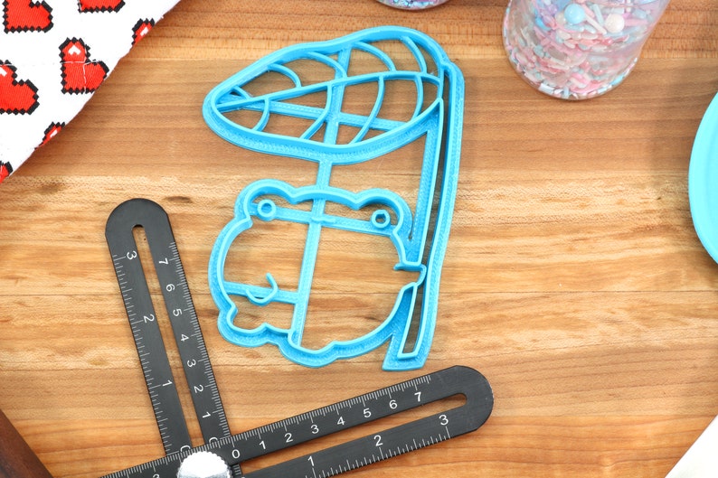 May include: A blue plastic cookie cutter shaped like a frog sitting under a leaf.