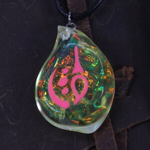 May include: A teardrop-shaped pendant necklace with a pink symbol inside. The pendant is made of clear resin with iridescent glitter embedded in it. The necklace is on a black cord.