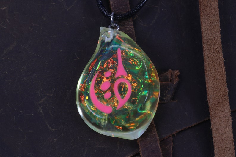 May include: A teardrop-shaped pendant necklace with a pink symbol inside. The pendant is made of clear resin with iridescent glitter embedded in it. The necklace is on a black cord.