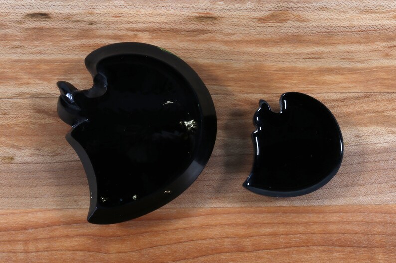May include: Two black resin crescent moon shapes, one larger than the other. The larger crescent moon has gold flecks embedded in the resin.