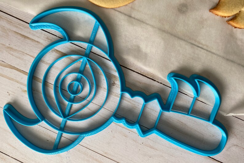Op de afbeelding: Een blauwe plastic koekjesvormer in de vorm van een gestileerde schorpioen met een gedetailleerd ontwerp.