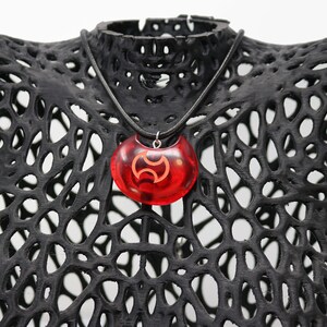 May include: A red resin pendant necklace with a black symbol. The necklace is on a black mannequin bust.