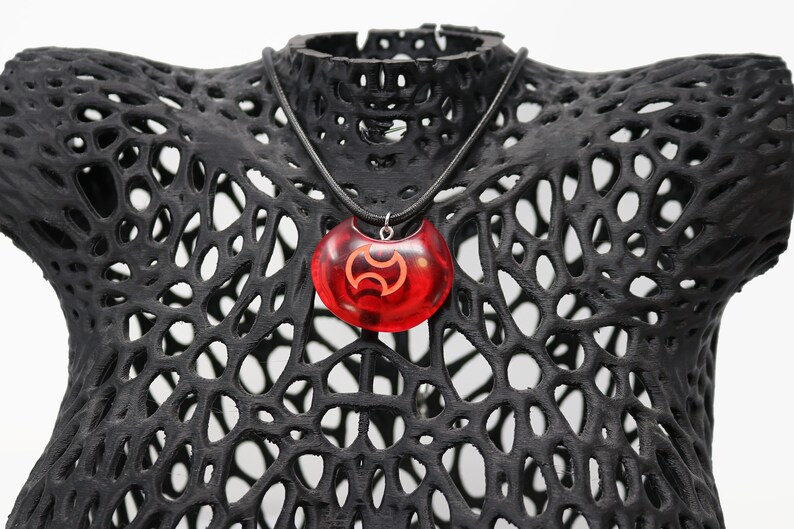 May include: A red resin pendant necklace with a black symbol. The necklace is on a black mannequin bust.