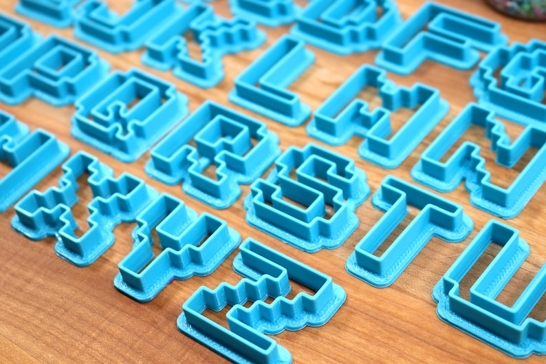 May include: A set of blue plastic cookie cutters shaped like letters of the alphabet in a pixelated style.