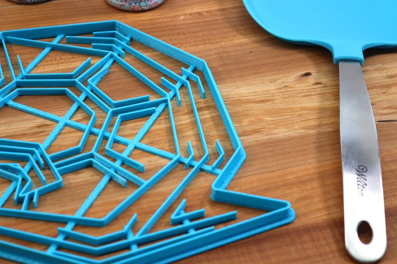 May include: A blue plastic snowflake cookie cutter on a wooden surface. A blue spatula with a silver handle is also in the image.