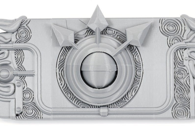 May include: A gray 3D printed box with a circular design and three arrow-shaped protrusions. The box has a textured surface and intricate details.