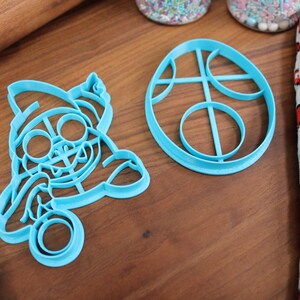 Op de afbeelding: Twee blauwe plastic koekjesvormen, een in de vorm van een cartoonfiguur en de andere in de vorm van een ei met cirkels erin.