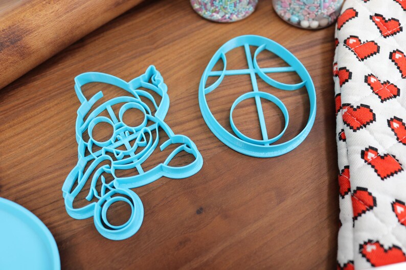 Op de afbeelding: Twee blauwe plastic koekjesvormen, een in de vorm van een cartoonfiguur en de andere in de vorm van een ei met cirkels erin.