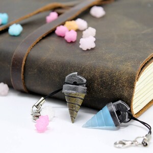 May include: Two keychains with drill bit charms. One charm is silver and gold, the other is blue. Both charms are attached to black cords with silver clasps.