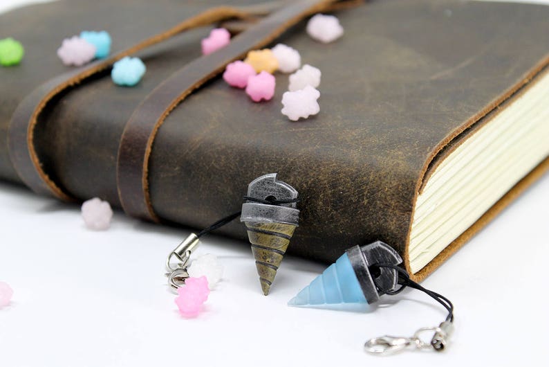 May include: Two keychains with drill bit charms. One charm is silver and gold, the other is blue. Both charms are attached to black cords with silver clasps.