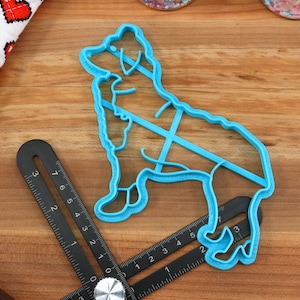 May include: A blue plastic cookie cutter shaped like a dog. The cutter is on a wooden surface with a black ruler.