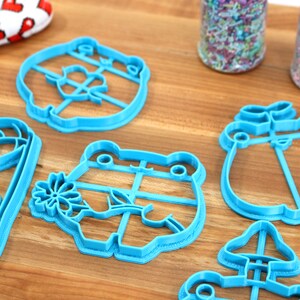 May include: A set of six blue plastic cookie cutters shaped like a frog, a mushroom, a bear, a penguin, a flower, and a house.
