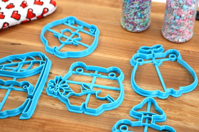 May include: A set of six blue plastic cookie cutters shaped like a frog, a mushroom, a bear, a penguin, a flower, and a house.