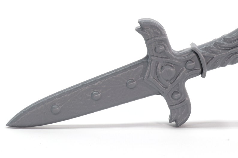 May include: A gray plastic dagger with a detailed, ornate handle. The blade is pointed and has a textured surface.