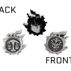May include: Three silver metal charms with a black and white design. The charms are shaped like a flame, a scale, and a flower. The back of the charms is blank. The front of the charms has a design on it. The charms are labeled "BACK" and "FRONT".
