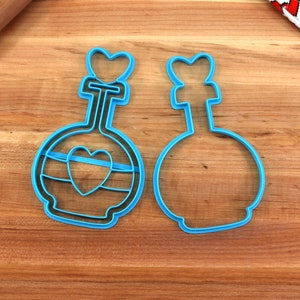 May include: Two blue plastic cookie cutters shaped like potion bottles with heart details. One cutter has a heart design on the bottle and the other is plain.
