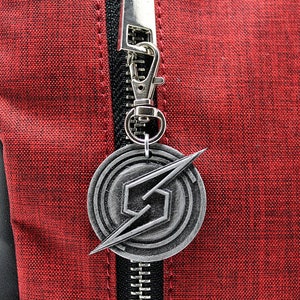 May include: A silver metal zipper charm with a stylized lightning bolt and a circular design. The charm is attached to a red backpack.