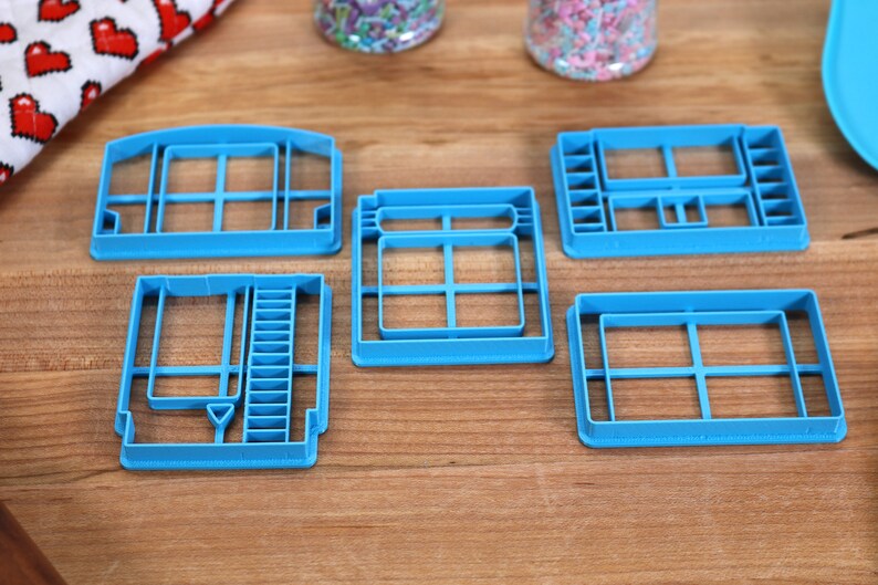 May include: Five blue plastic cookie cutters shaped like different video game cartridges.