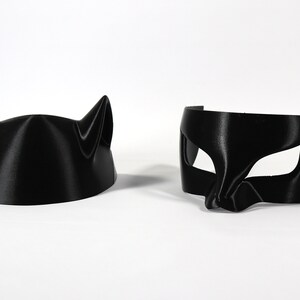 May include: Two black cat masks, one with ears and the other with a more traditional eye mask design.