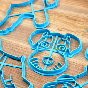 May include: A set of five blue plastic cookie cutters shaped like dogs. The cutters are on a wooden surface.
