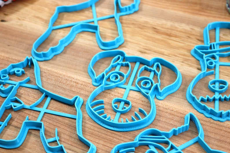 May include: A set of five blue plastic cookie cutters shaped like dogs. The cutters are on a wooden surface.