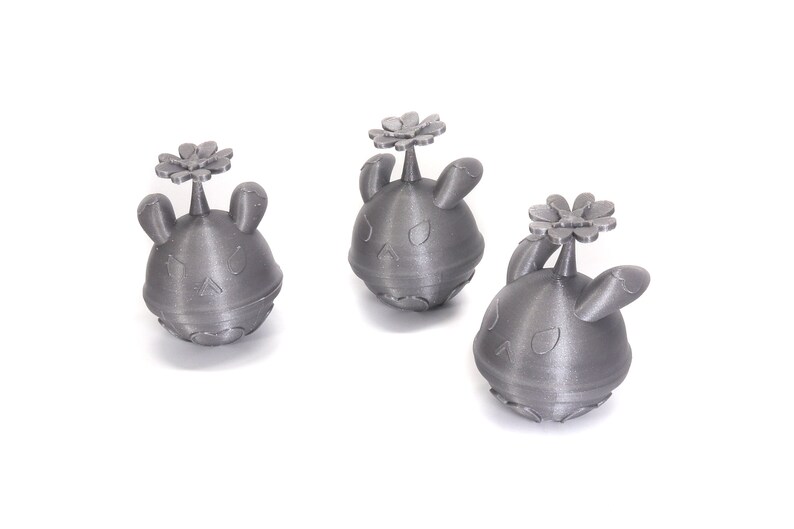 May include: Three silver-colored 3D printed figurines of a cartoon character with a flower on top. The character has a round body, two ears, and a face with eyes and a mouth.
