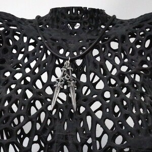May include: A silver pendant necklace featuring two sword charms. The necklace is displayed on a black, open-weave bust form. The swords have ornate handles and pointed blades. The bust form has a unique, porous design.