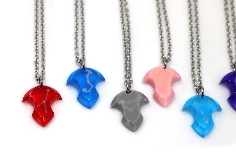 Puede incluir: Seis collares de plata con colgantes de diferentes colores. Cada colgante tiene forma de l&aacute;grima con un dise&ntilde;o de constelaci&oacute;n en el interior. Los colgantes son rojo, azul, gris, rosa, azul claro y morado.