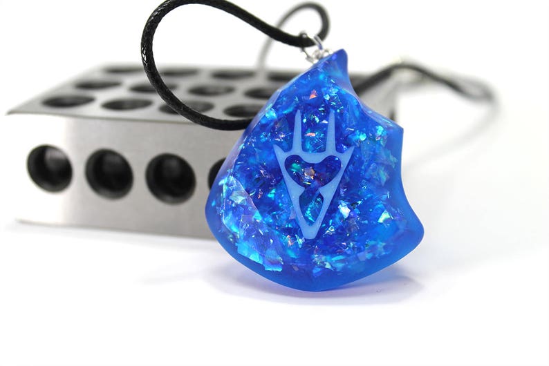 May include: A blue resin pendant necklace with a white hand-shaped design and iridescent glitter embedded in the resin. The pendant is shaped like a jagged rock.