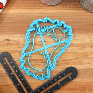 May include: A blue plastic cookie cutter shaped like a footprint with a jagged edge. The cutter is on a wooden surface.