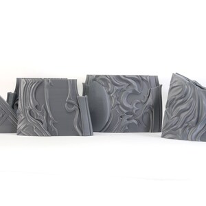 May include: Four gray 3D printed pieces of a decorative wall panel with a swirling, ornate design.