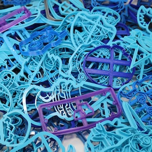 Op de afbeelding: Een grote verzameling blauwe en paarse plastic koekjesvormen in verschillende vormen en maten. De vormen zijn in een willekeurige stapel gerangschikt.