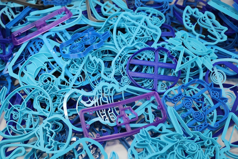 Op de afbeelding: Een grote verzameling blauwe en paarse plastic koekjesvormen in verschillende vormen en maten. De vormen zijn in een willekeurige stapel gerangschikt.