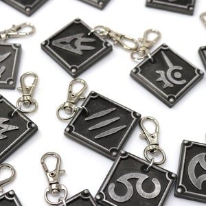 May include: A set of 10 silver keychains with different symbols on each. The keychains are square shaped and have a silver metal finish. The symbols are all different and include a sword, a flame, a circle with a line through it, and a circle with a line through it.
