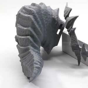 May include: A gray 3D printed dragon head sculpture with detailed scales and horns. The sculpture is broken into multiple pieces and is laying on a white surface.