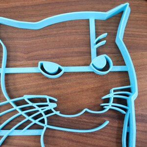 May include: A light blue plastic cat-shaped cookie cutter with a detailed design of eyes, whiskers, and a mouth.