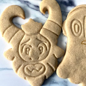 K&ouml;nnte beinhalten: Zwei Zuckerkekse, die mit Zuckerguss verziert sind. Ein Keks ist in Form eines Geistes mit zwei gro&szlig;en Augen und einem kleinen Mund. Der andere Keks ist in Form eines Monsters mit H&ouml;rnern, gro&szlig;en Augen und einem gro&szlig;en Mund.