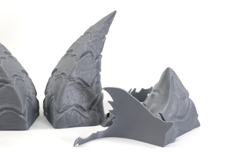 Op de afbeelding: Drie grijze 3D-geprinte stukken van een drakenkop, een is een grote hoorn, een is een kleinere hoorn en de derde is de kaak met tanden.