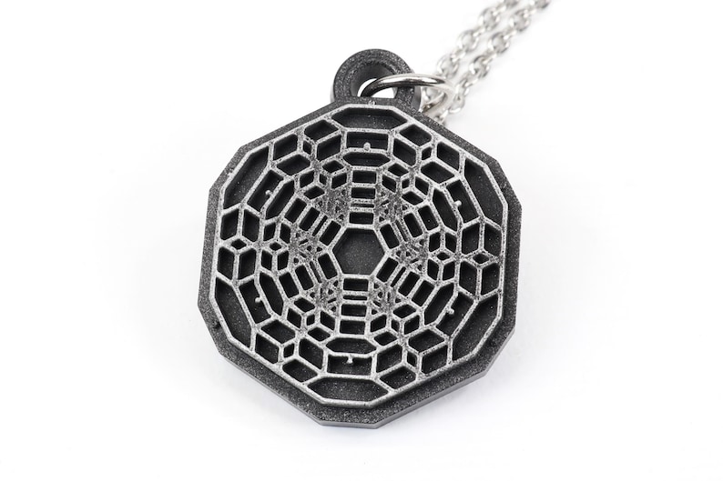 May include: A silver-toned pendant necklace featuring a geometric, octagonal design with a detailed, intricate pattern. The pendant is made of metal and has a matte finish.